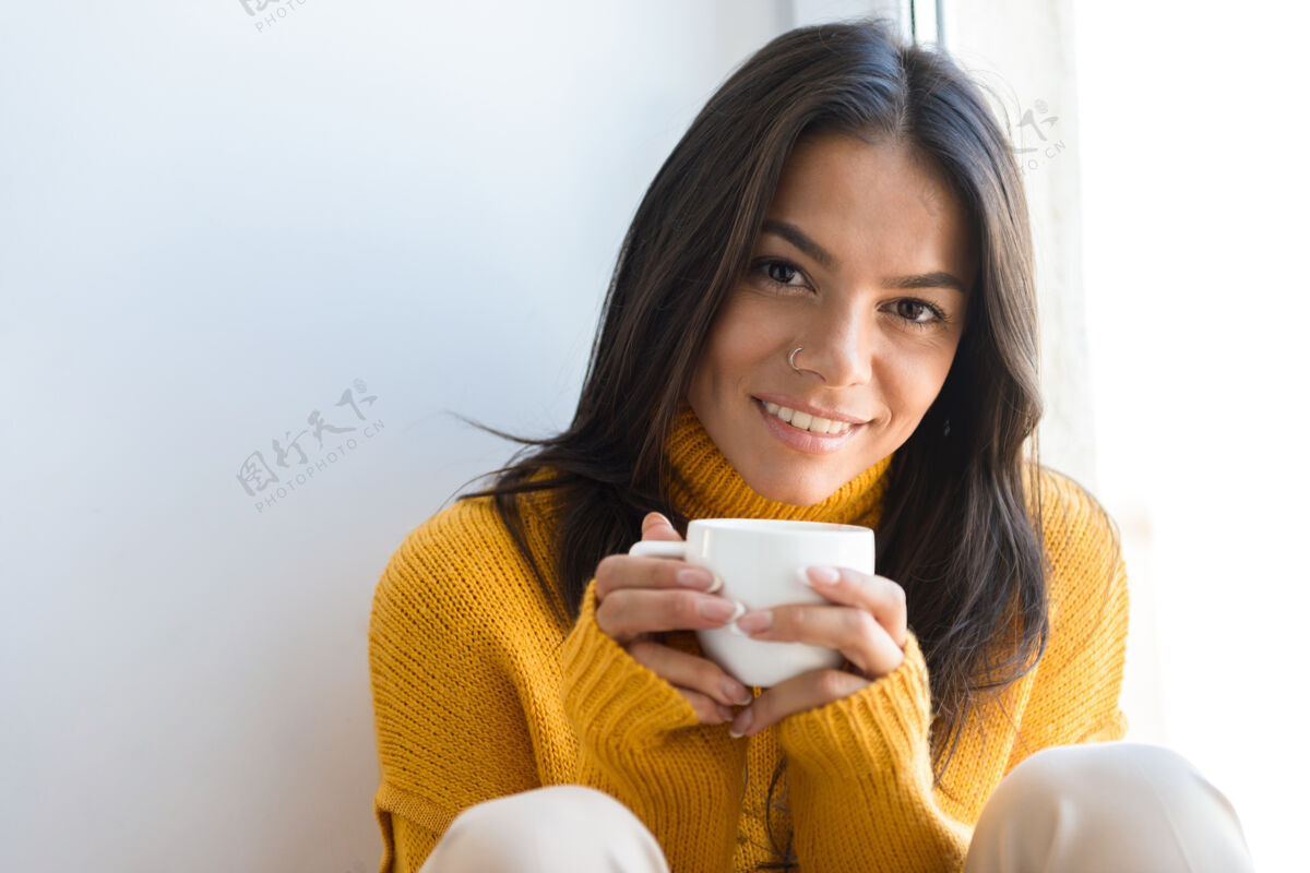 秋天特写一个微笑的年轻女子穿着毛衣坐在窗前 拿着一杯茶女舒适饮料