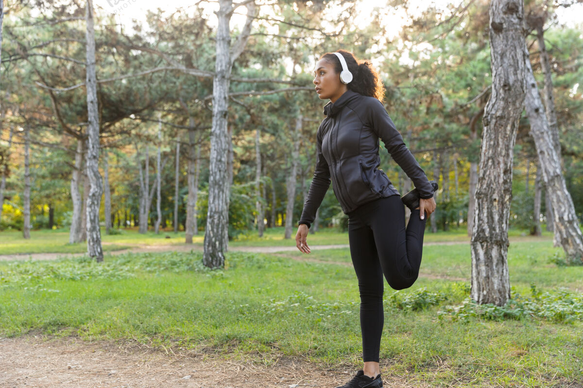 锻炼20多岁的年轻女子穿着黑色运动服 在绿色公园里伸展身体伸展非洲无线