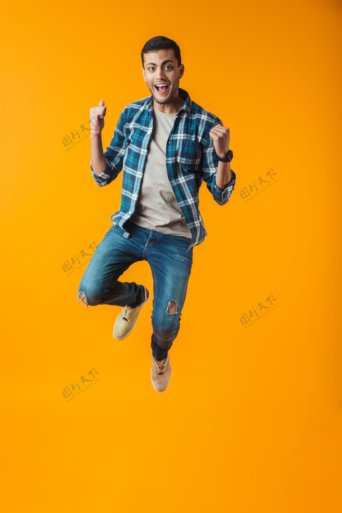 姿势一个穿着格子衬衫的快乐的年轻人的全长肖像被隔离在橙色的墙上 跳跃庆祝成功格子看充分