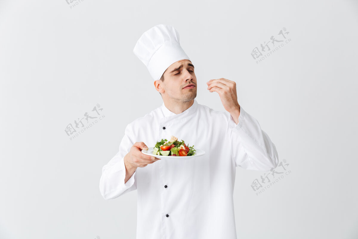 午餐严肃的男厨师穿着制服 在白色墙壁上的盘子上展示新鲜的蔬菜沙拉菜肴专业职业