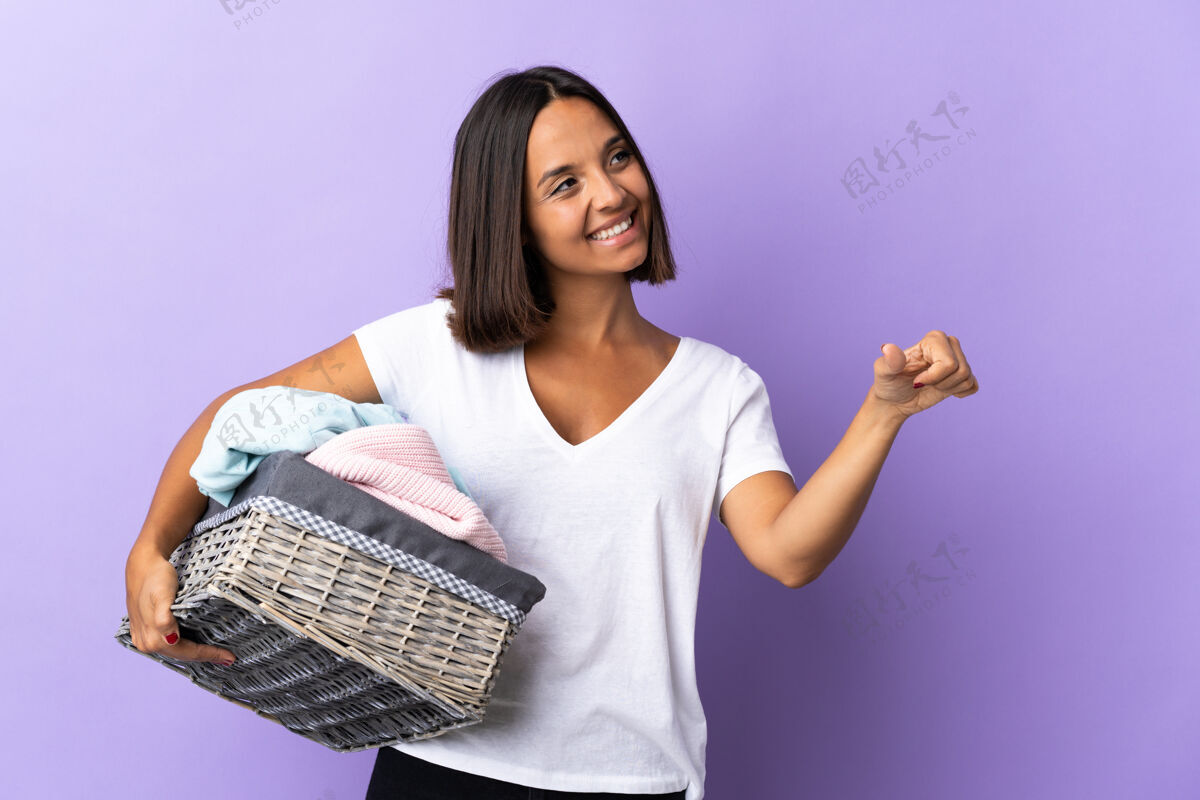批准一个年轻的拉丁女人拿着一个衣服篮子 孤立地站在紫色地上 竖起大拇指拇指年轻好