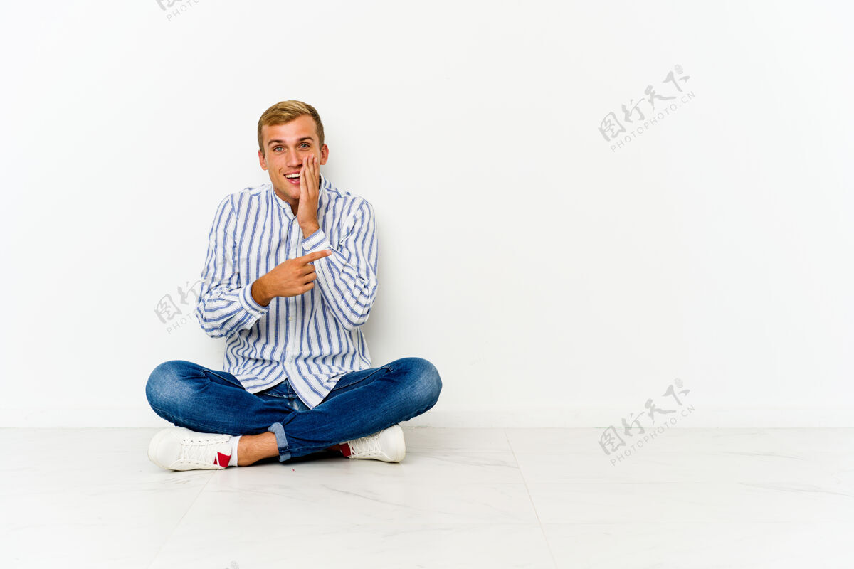 男人年轻的白种人坐在地板上说闲话 指着旁边的报道报道男人秘密