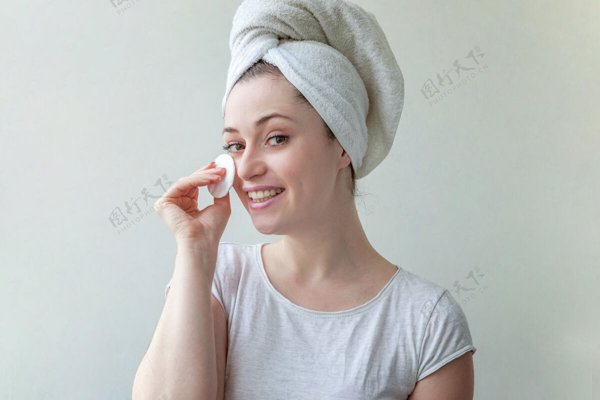 擦拭头上戴着毛巾的微笑女人的美丽肖像 柔软健康的皮肤 用隔离在白色背景上的化妆棉卸妆毛巾洗制造