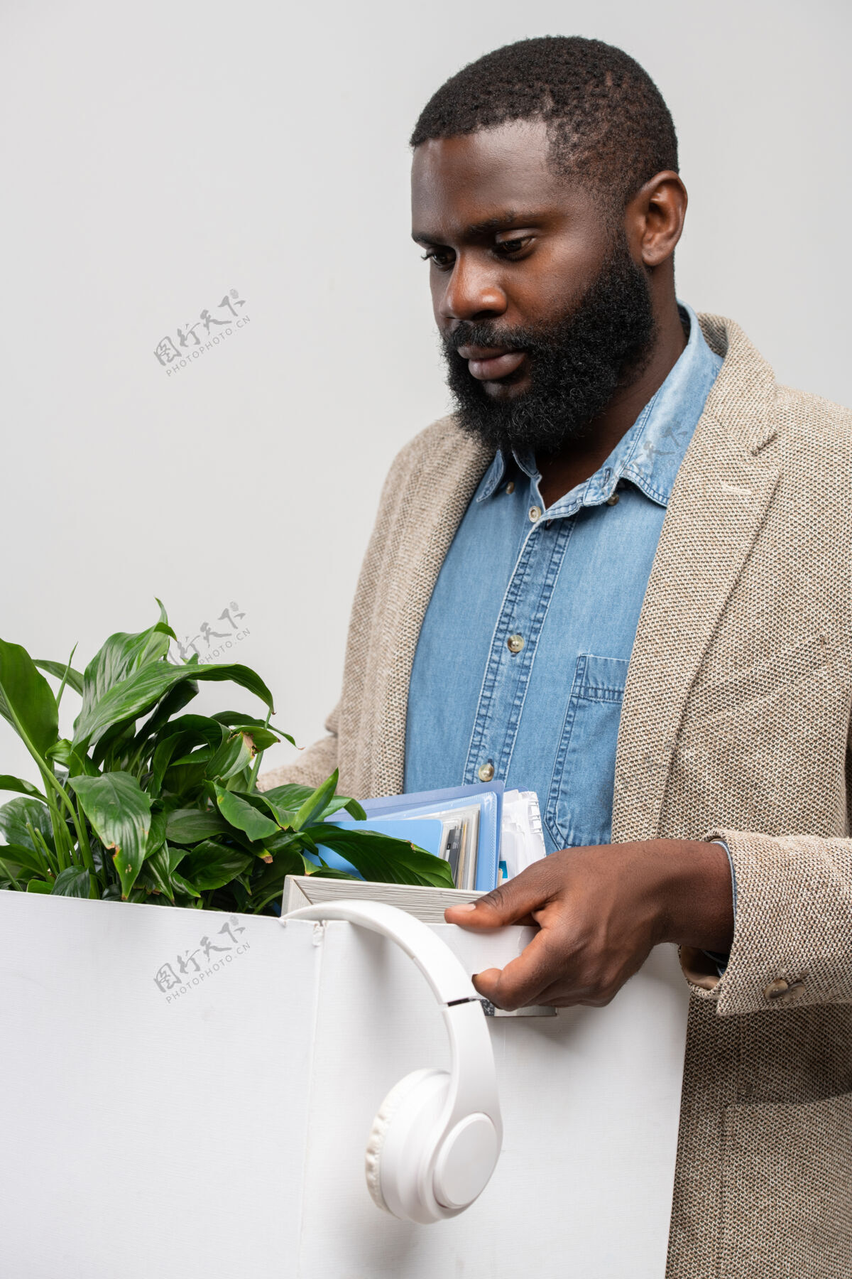 休闲服年轻的被解雇的非洲裔办公室经理在离开工作场所时悲伤地看着带着耳机 绿色植物和其他用品的盒子成人肖像投票