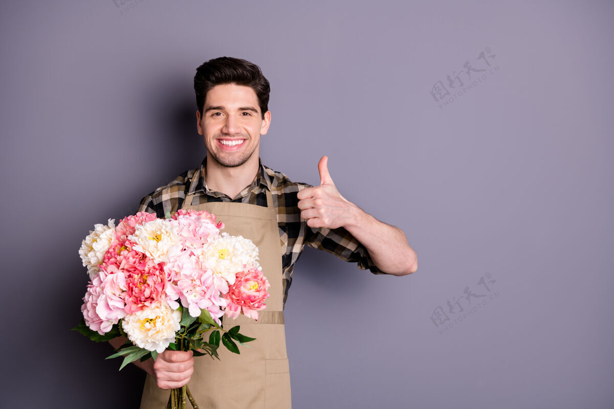 商店穿着格子衬衫的开朗帅哥竖起大拇指的照片 对花店孤立的灰色墙壁留下反馈花束批准花店