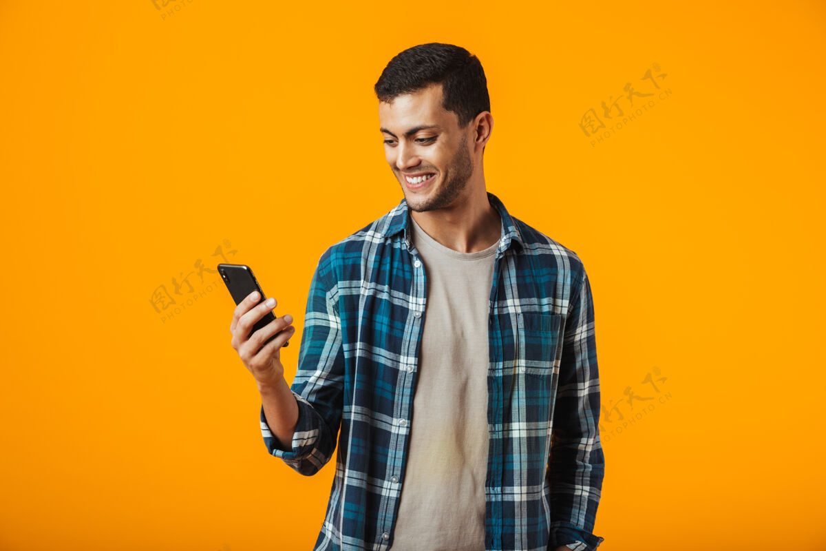 年轻一个穿着格子衬衫的年轻人孤零零地站在橘色的墙上 用着手机通信英俊站