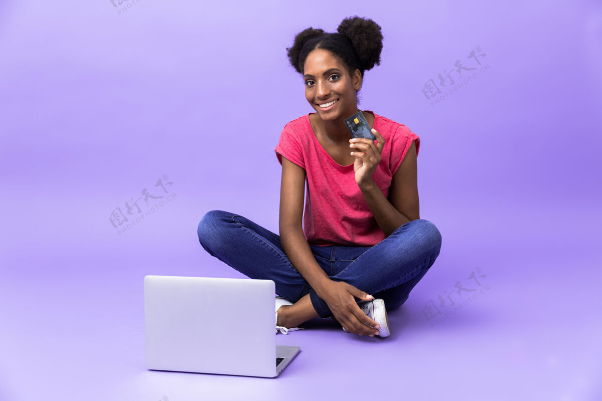 微笑坦率的非洲裔美国妇女微笑着使用银色笔记本电脑 而坐在地板上双腿交叉 孤立内容美国喜悦