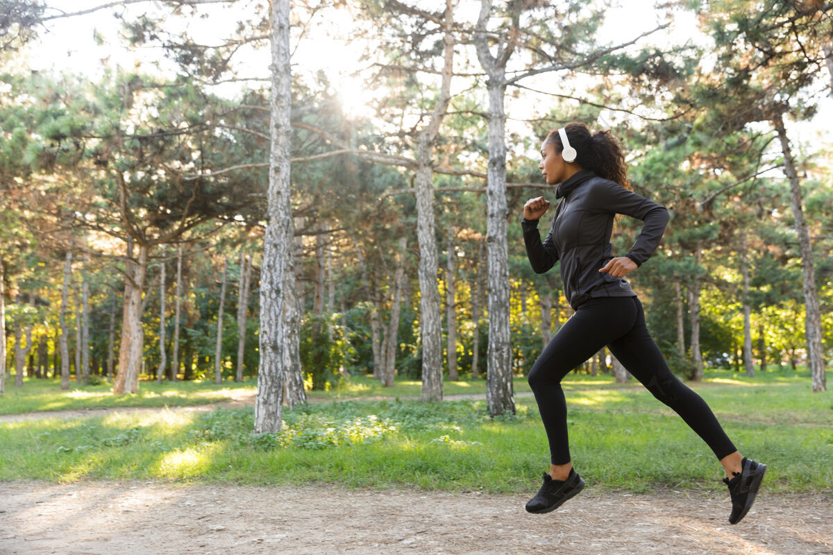 吸引力一张20多岁的女运动员穿着黑色运动服 戴着耳机 在绿色公园里跑步的照片女性耳机保健