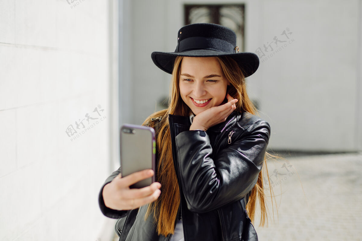 女人户外夏日写真的年轻时尚女孩在阳光明媚的日子摆在街上与手机移动短信时髦