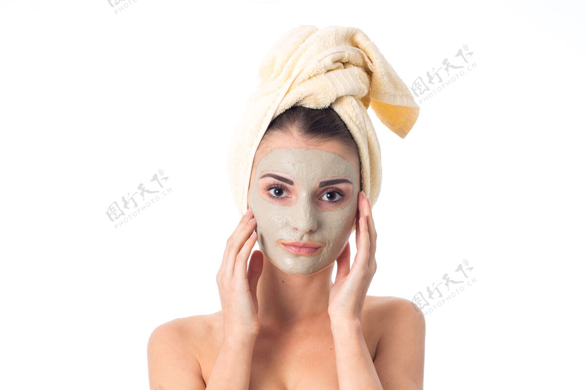 成人年轻的女人用洁面面膜和毛巾在脸上护理她的皮肤隔离在白色的墙壁上美丽女人年轻