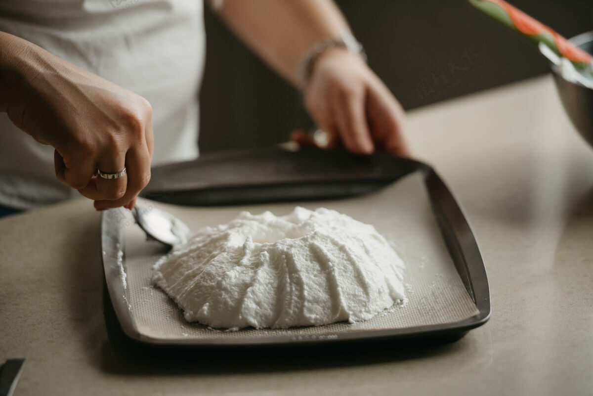 配料一位年轻女子的手的近照 她用勺子在托盘上制作了一个大蛋白酥皮的形状特写白人搅拌机