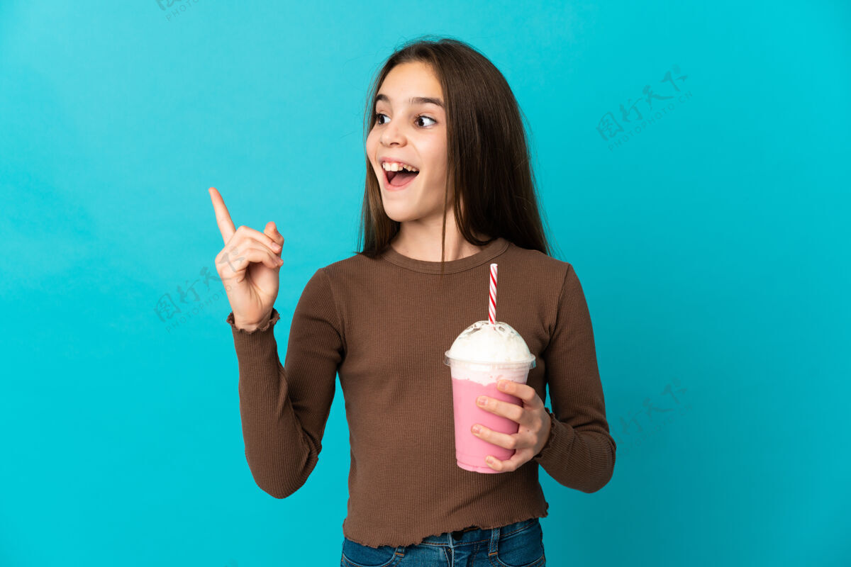 刷新拿着草莓奶昔的小女孩孤零零地站在蓝色的墙上 一边举起一根手指 一边想实现解决方案女孩奶昔思考