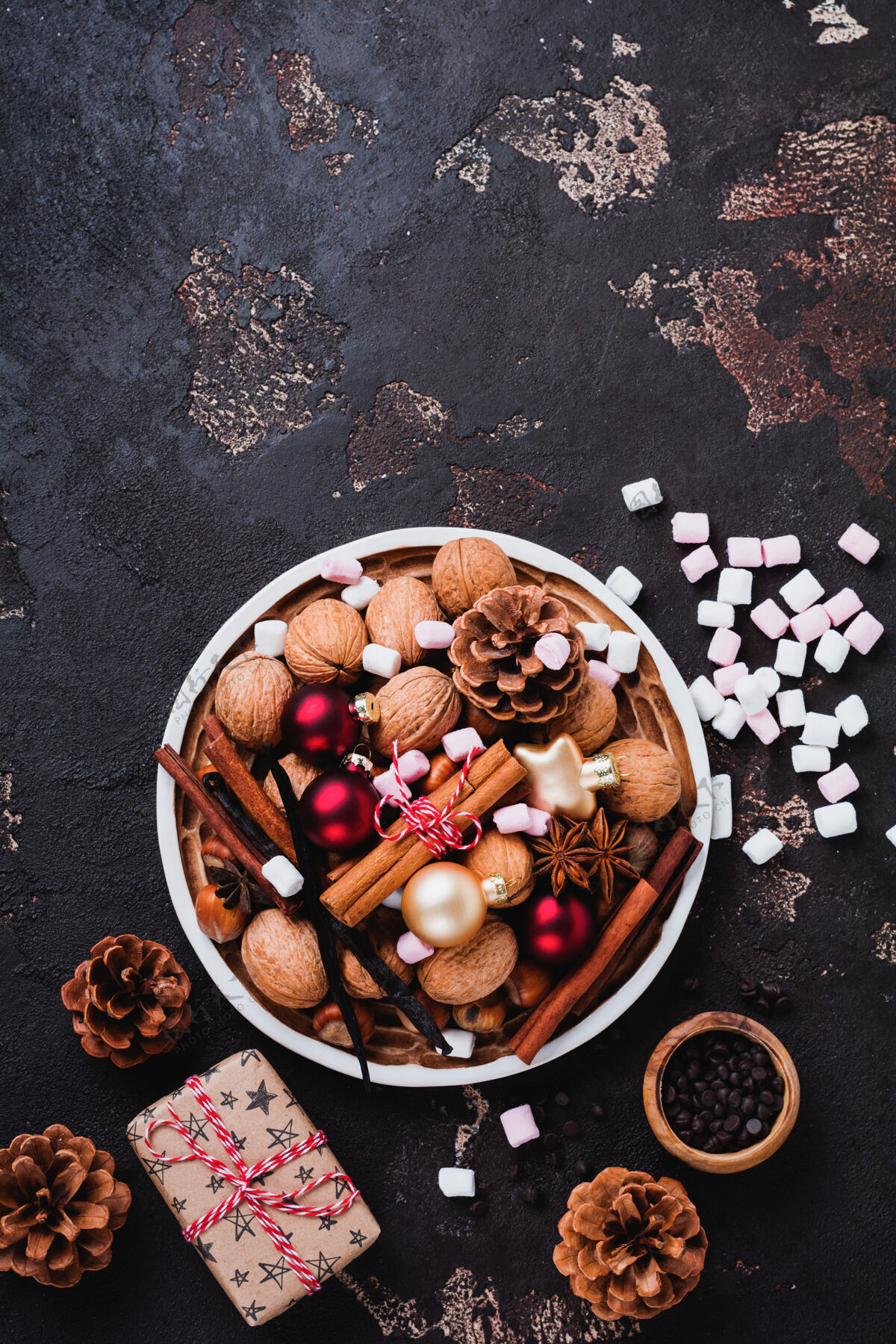 混合混合健康的生榛子和核桃 肉桂棒 八角 香草 巧克力和圣诞玩具在陶瓷板上棕色混凝土表面香草明信片食物