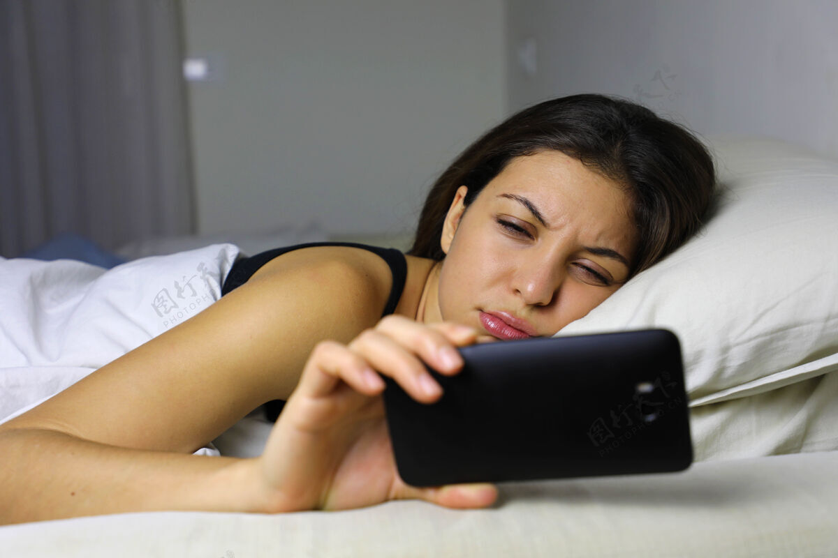 年轻失望悲伤的女人晚上躺在床上看手机上瘾短信不开心