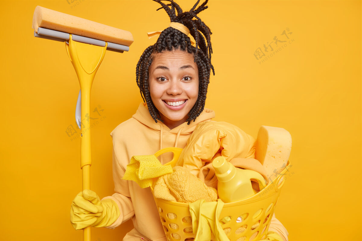 橡胶家庭主妇忙着做家务 在节前打扫房子 拿着拖把 提着洗衣篮 心情很好 被隔离在黄色上阳性洗涤剂女性