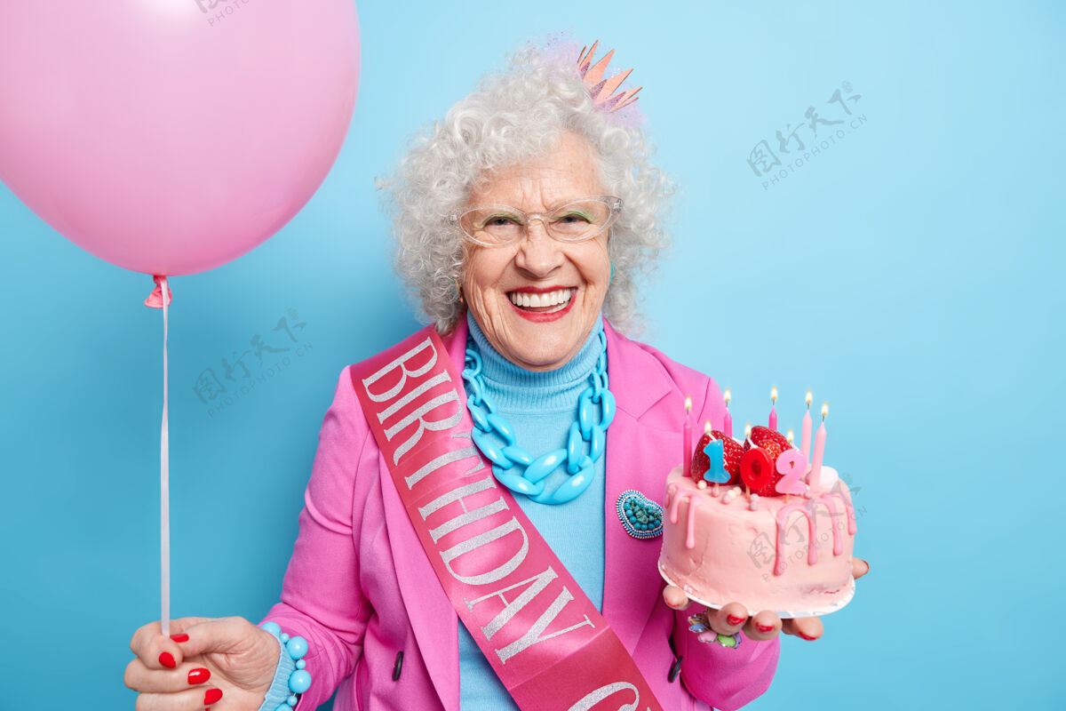 退休正面白发女子画像庆祝102岁生日 手持美味蛋糕和充气气球牙齿眼镜丝带