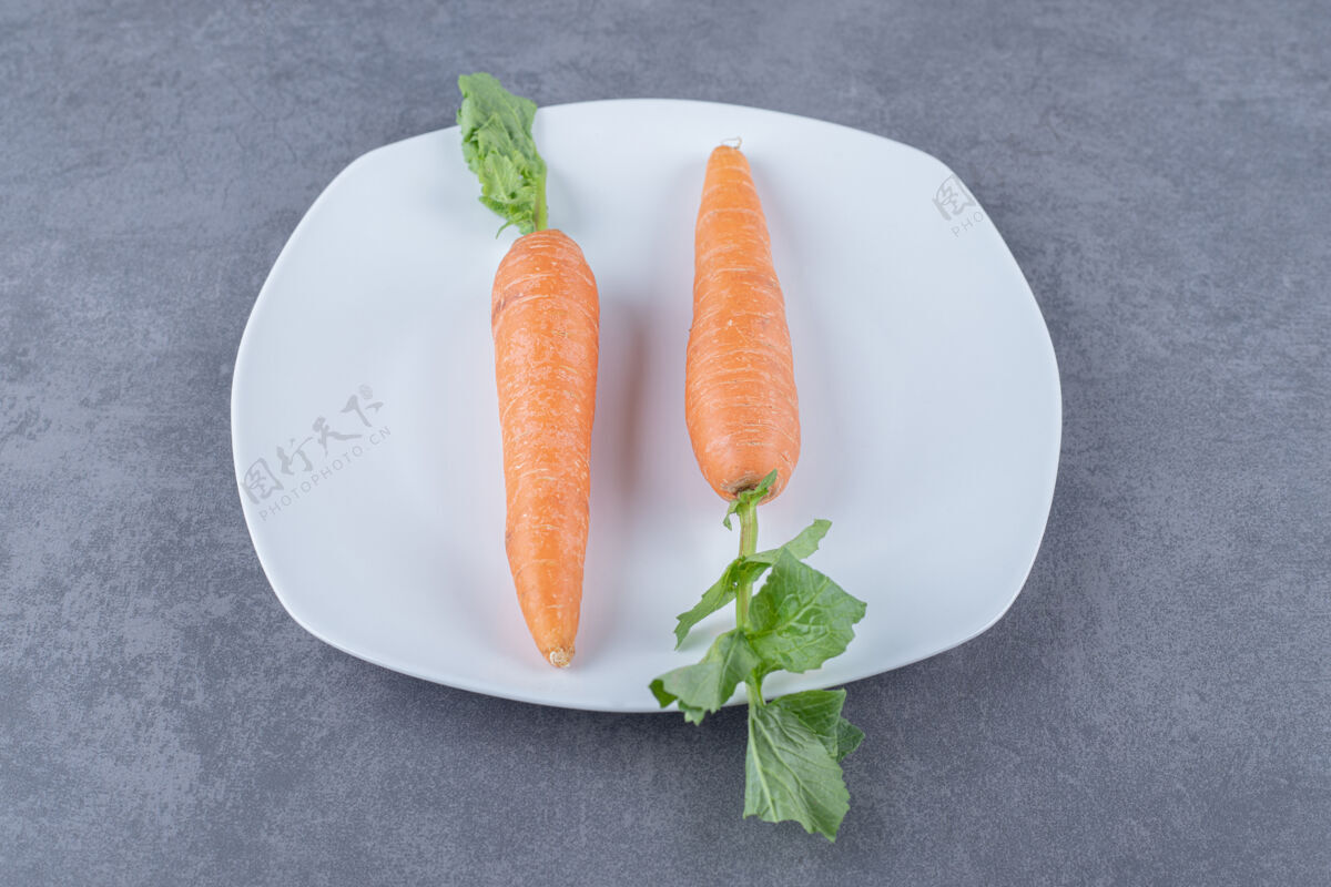 胡萝卜两个胡萝卜放在一个盘子里 放在大理石表面上有味道的好吃美味