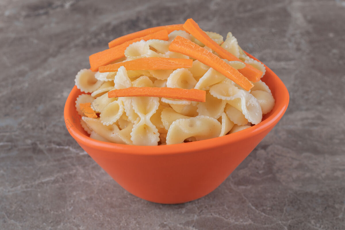 美味胡萝卜切碎放在碗里的意大利面上 放在大理石表面上可口有机营养