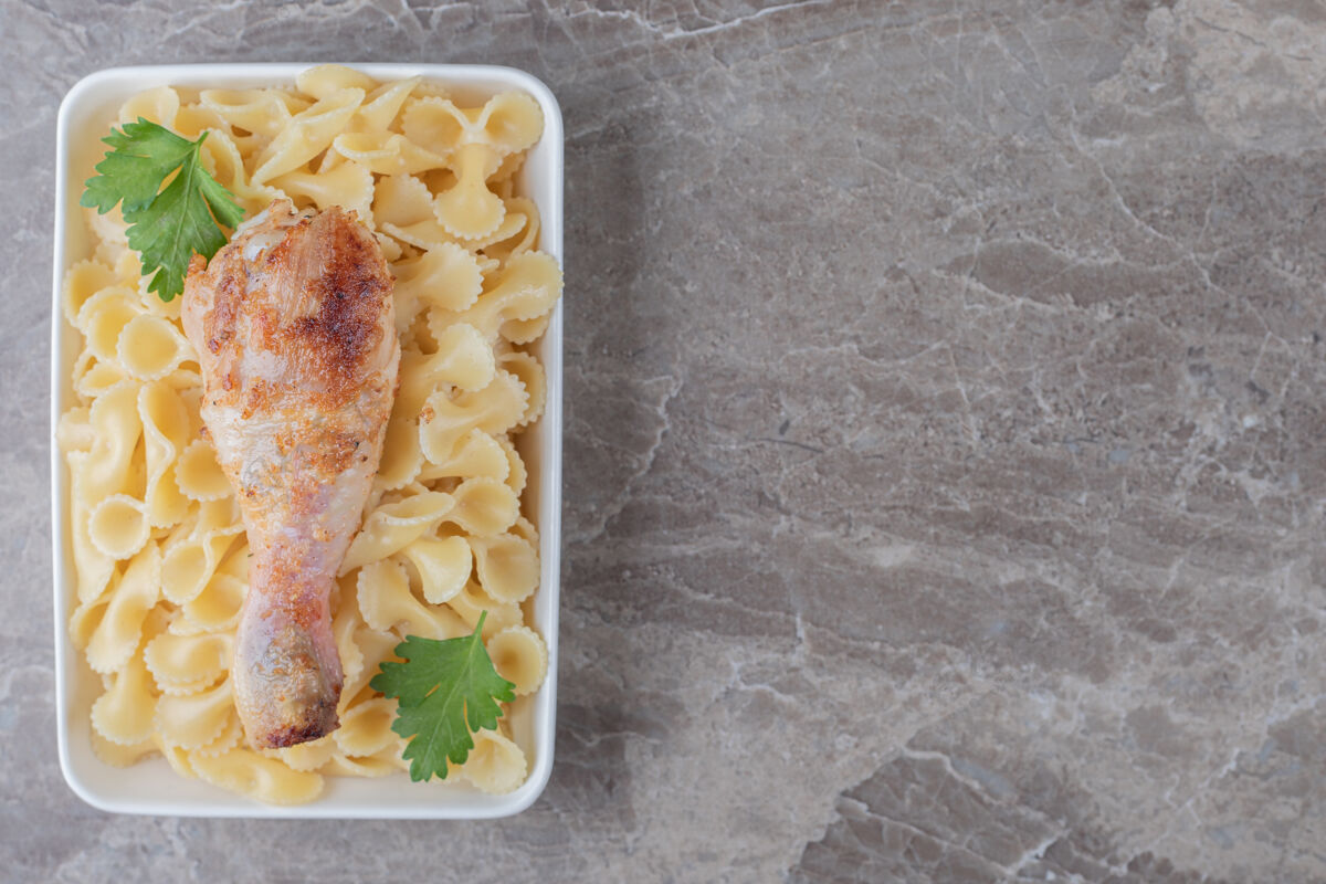 美味鸡肉鸡腿放在碗里的意大利面上 大理石背景上鸡腿风味背景