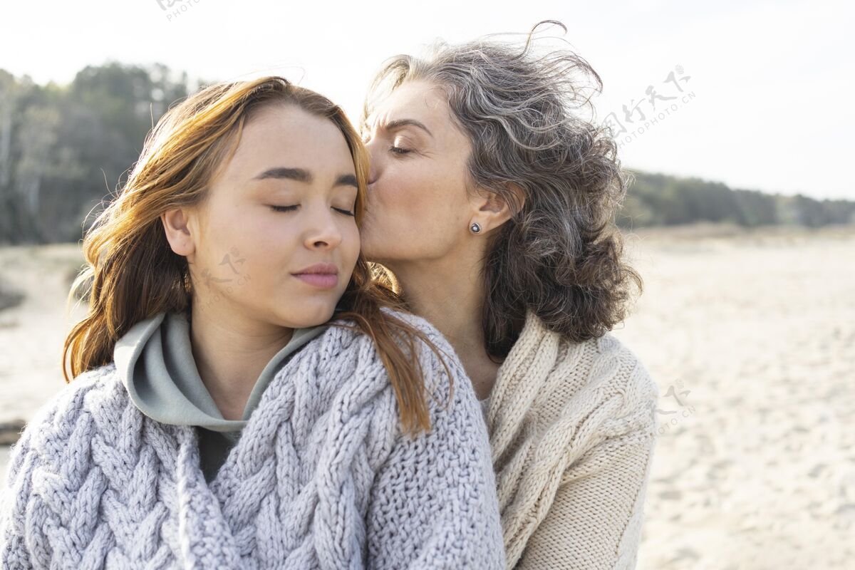 水平妈妈在沙滩上亲吻她的女儿女人家庭债券