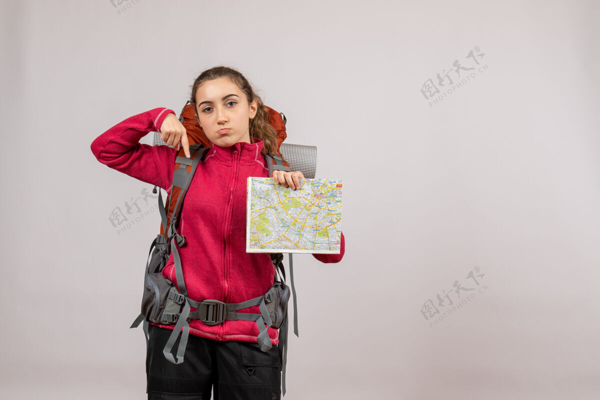 旅行者正面图：年轻的旅行者背着大背包 拿着地图指向下面旅游人女人