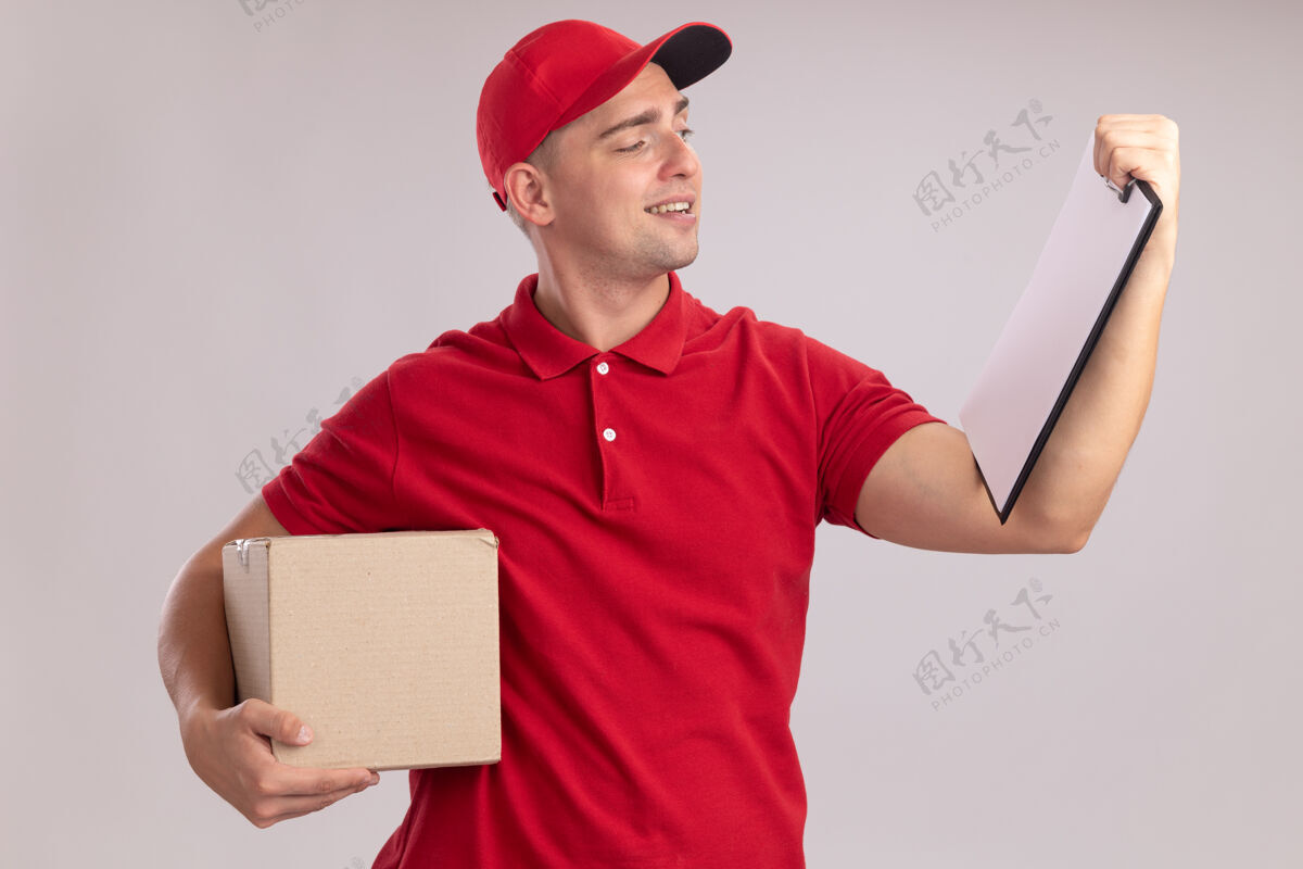 手高兴的年轻送货员穿着制服 拿着帽子盒 看着他手里的剪贴板孤立在白墙上帽子衣服制服