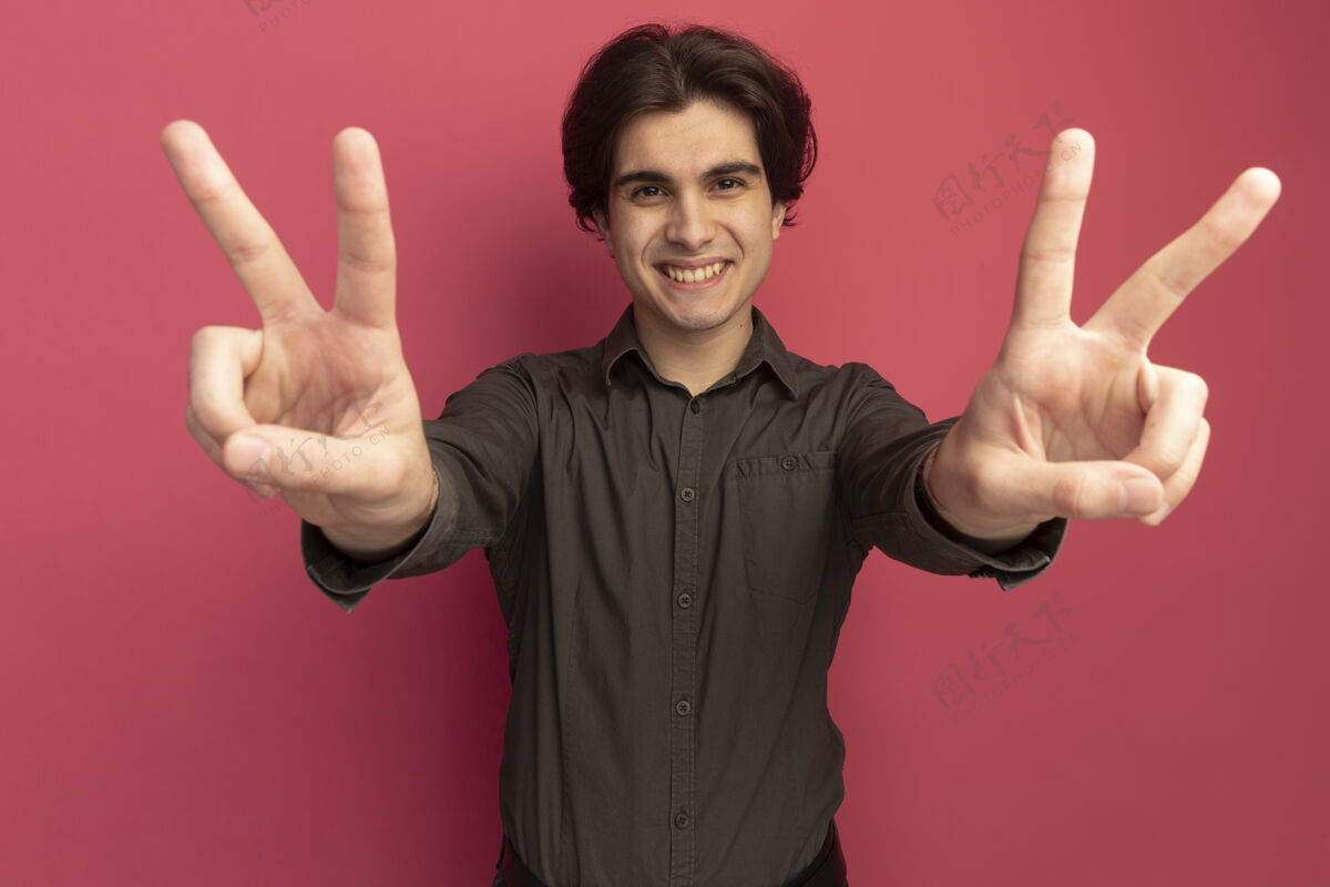 微笑面带微笑的年轻帅哥穿着黑色t恤 在粉红色的墙上显示出和平的姿态手势市民年轻