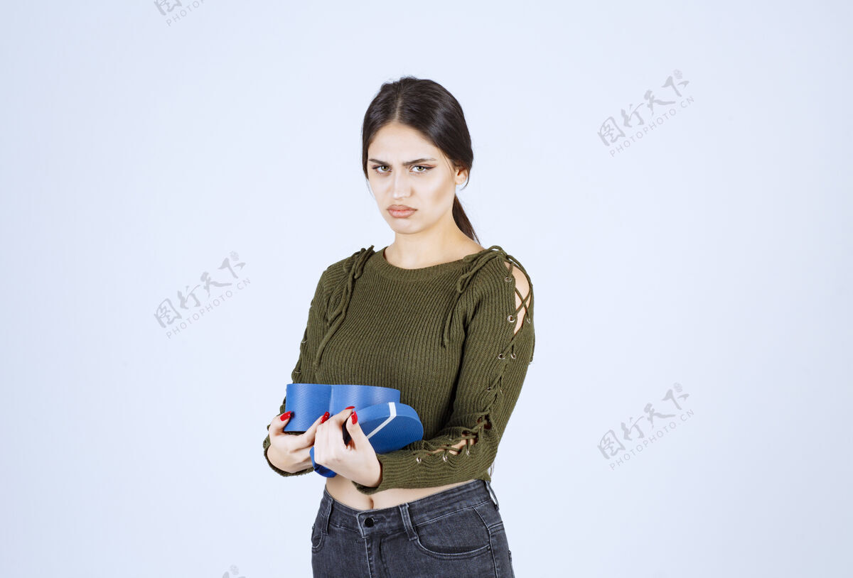 礼物手持蓝色礼盒的年轻女子 在白色背景上带着愤怒的表情持有惊喜女孩