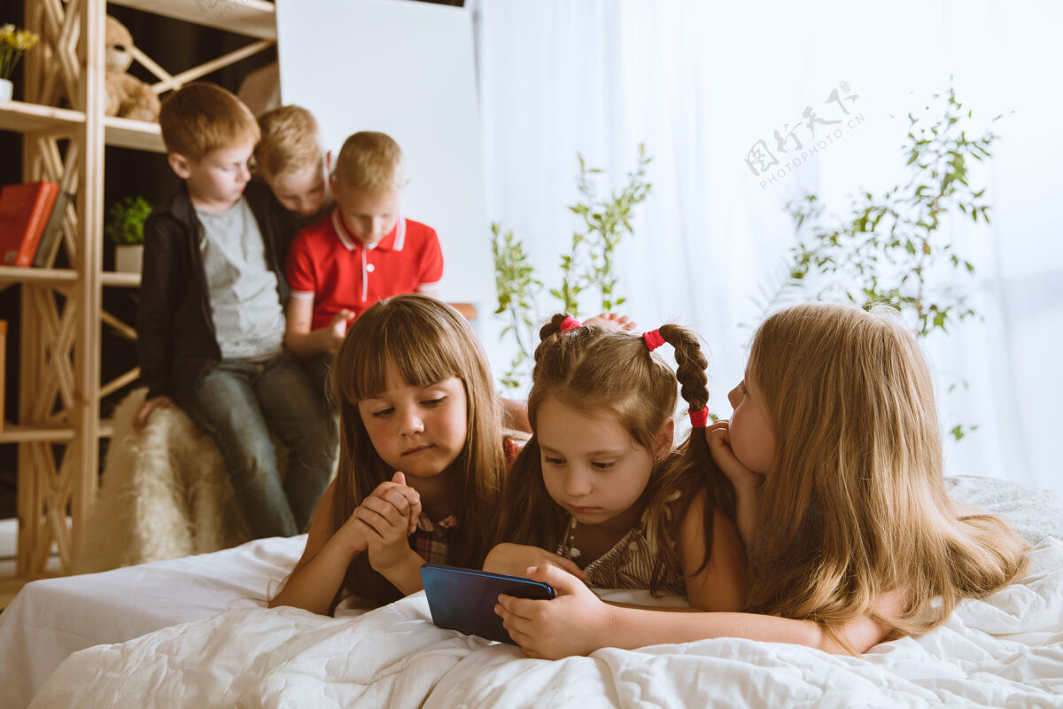 肖像男孩和女孩在家里使用不同的小玩意孩子们带着智能手表 智能手机和耳机自拍 聊天 游戏 看视频孩子们和现代科技的互动孩子青少年上瘾