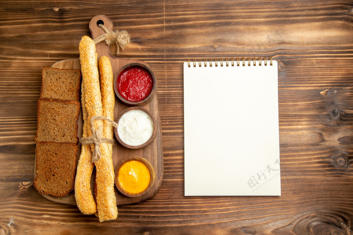 面包顶视图黑面包面包与面包记事本和调味品棕色办公桌上的食物面包面包面包辛辣美味盘子小吃