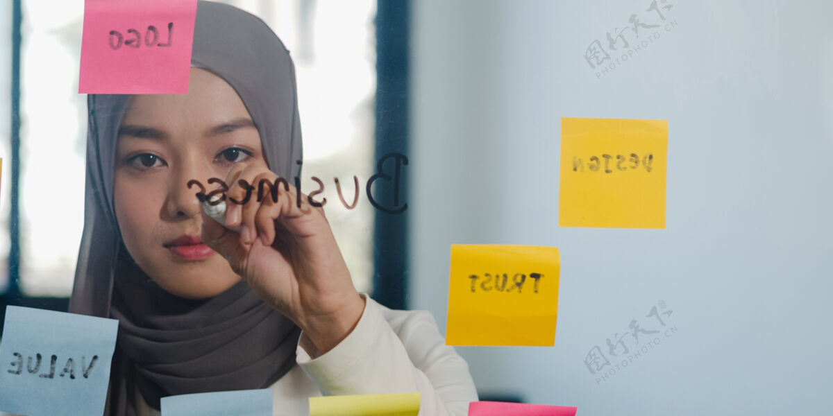 写作亚洲穆斯林女士在新常态办公室的玻璃板上写信息 策略 提醒年轻马来西亚办公室