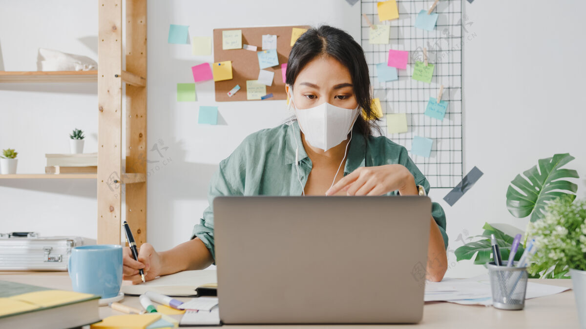 保护戴着医用口罩的亚洲女商人在起居室工作时 用笔记本电脑和同事通过视频通话的方式谈论这个计划流行病远程新常态