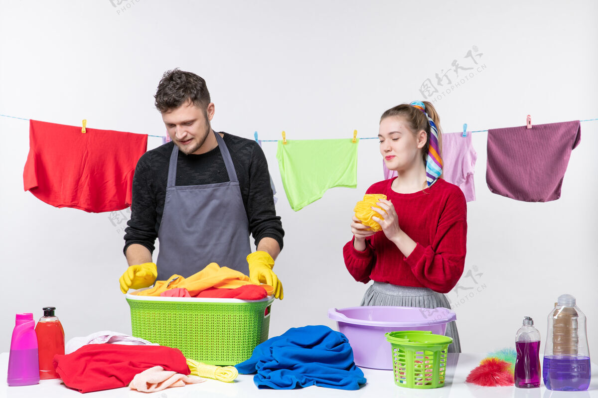 成人正面图有趣的年轻夫妇男人拿着洗衣篮 妻子拿着浴巾在白墙上购物人孩子