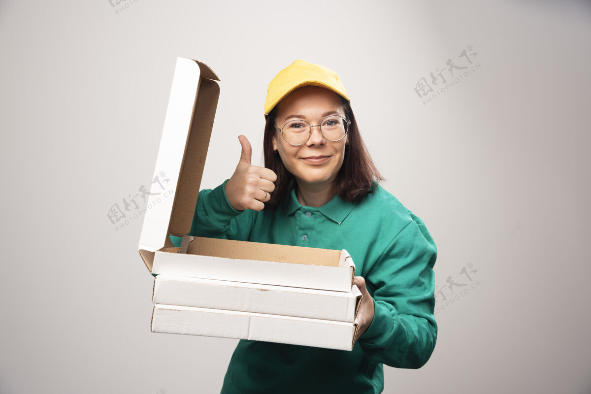帽子女送货员竖起大拇指 拿着一张白色的高质量照片上的比萨饼卡片女性女士表演