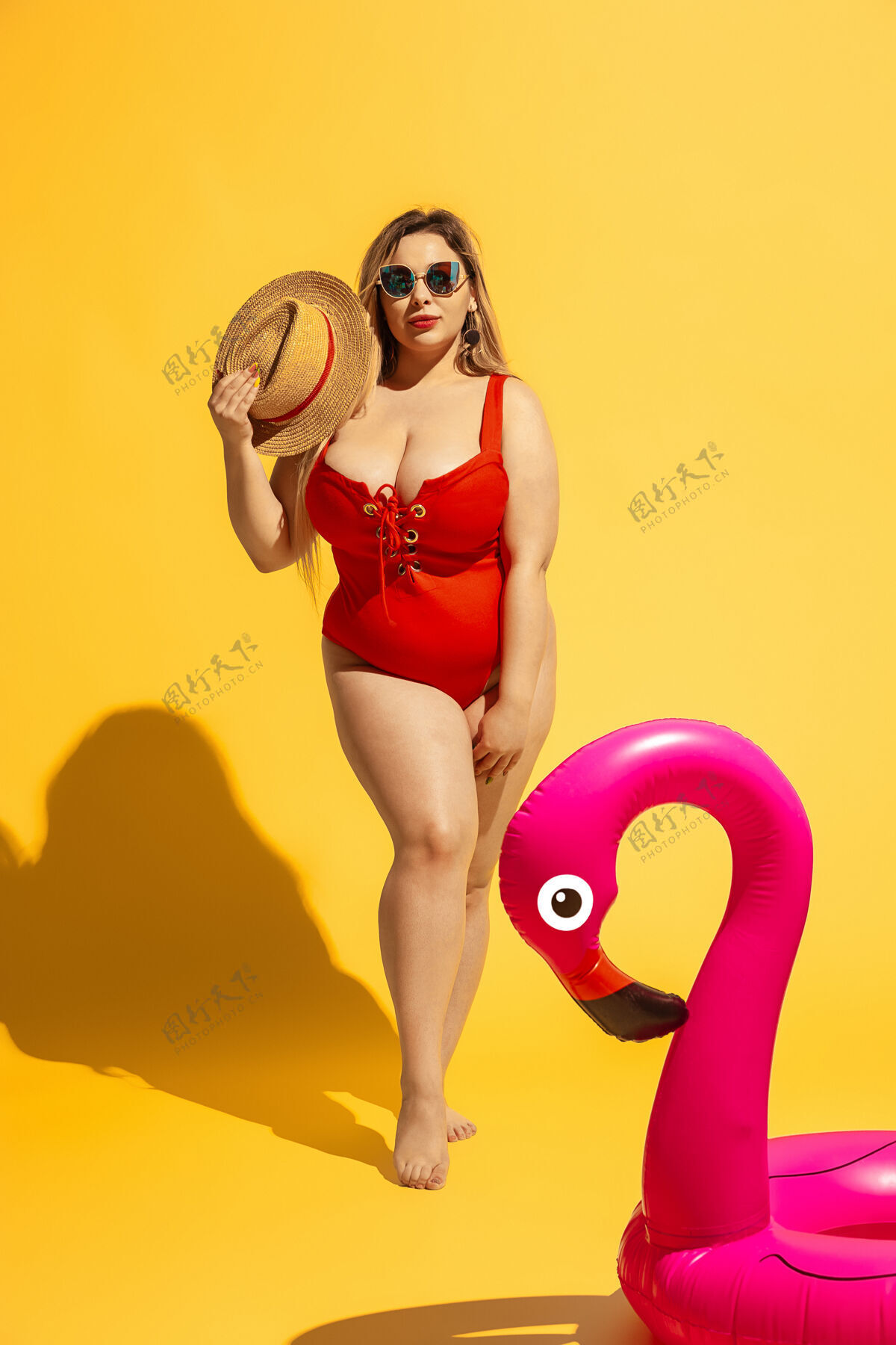 手臂年轻的白人大号女模特在黄墙上准备度假穿着红色泳衣和帽子的女人在游泳努力专业女性