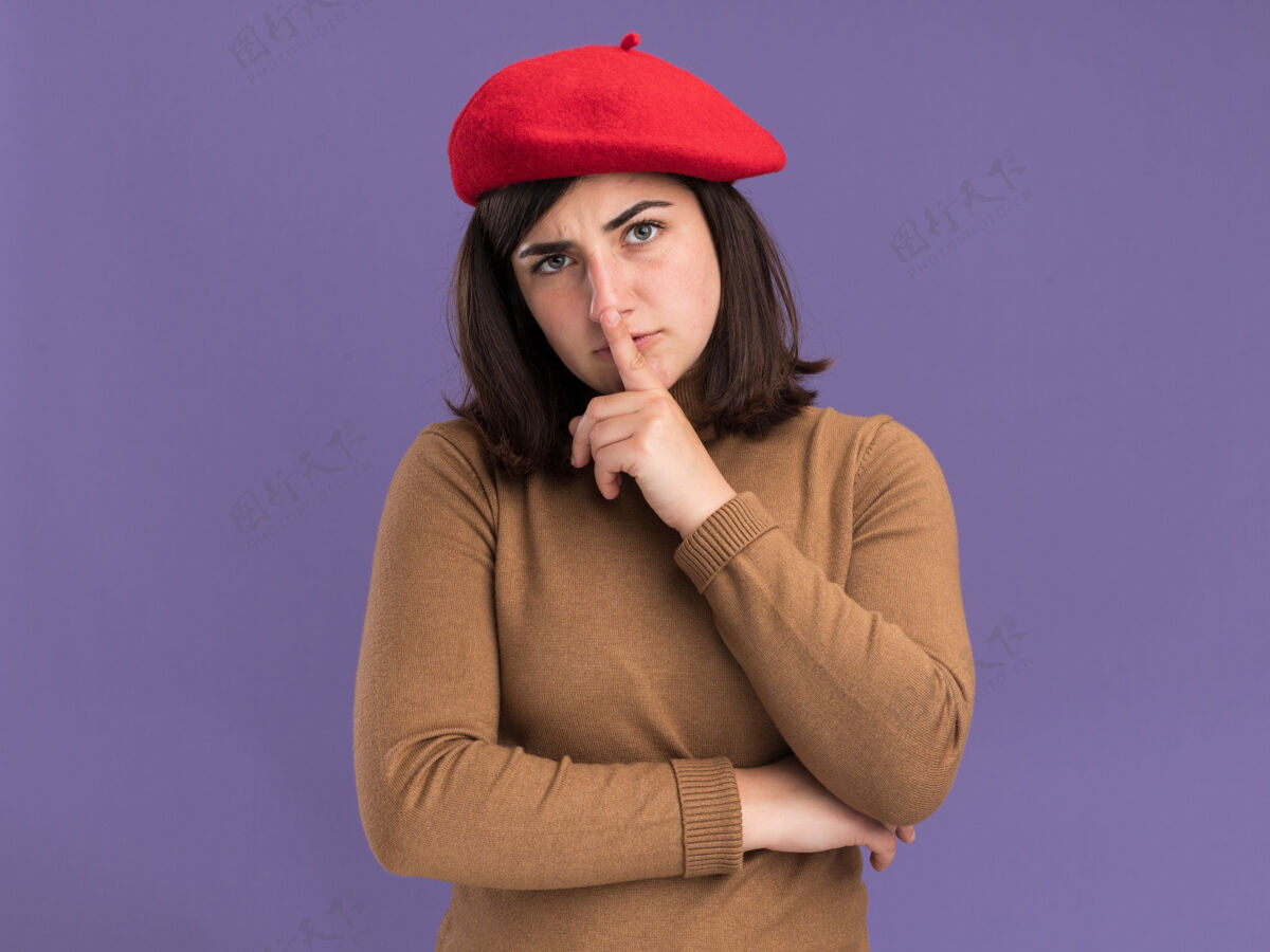 姿态自信的年轻漂亮白人女孩戴着贝雷帽做着沉默的手势紫色自信美丽