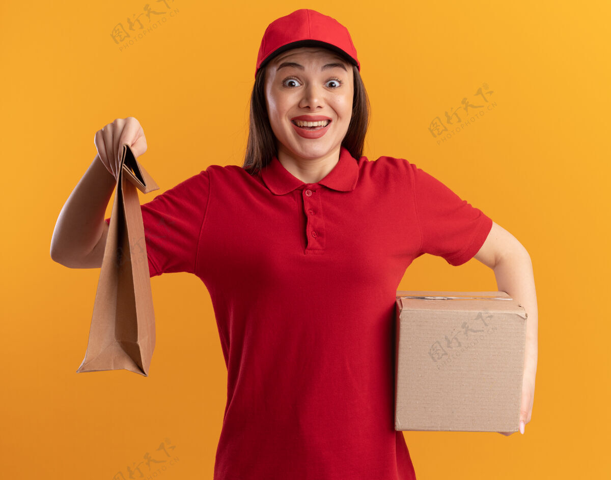 橘子穿着制服的兴奋漂亮的女送货员拿着纸包和名片盒名片盒拿着纸
