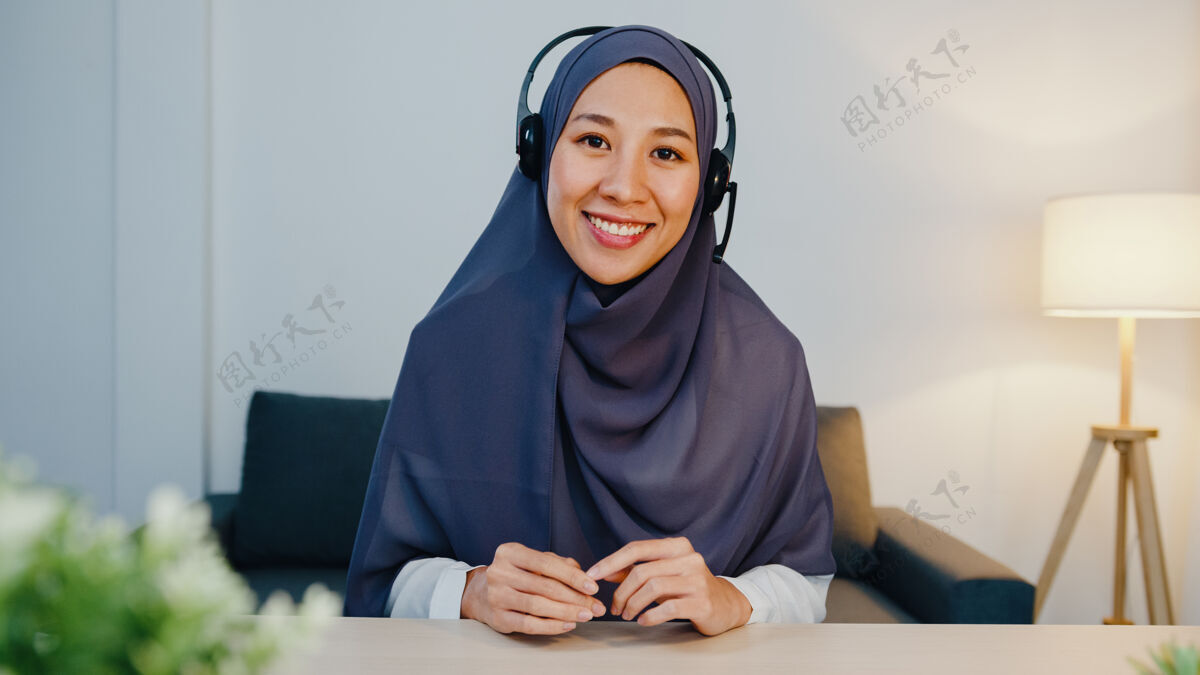 穆斯林穆斯林女士戴着耳机 用笔记本电脑 晚上在家办公的时候 在电话会议上和同事谈论销售报告头巾人员工作