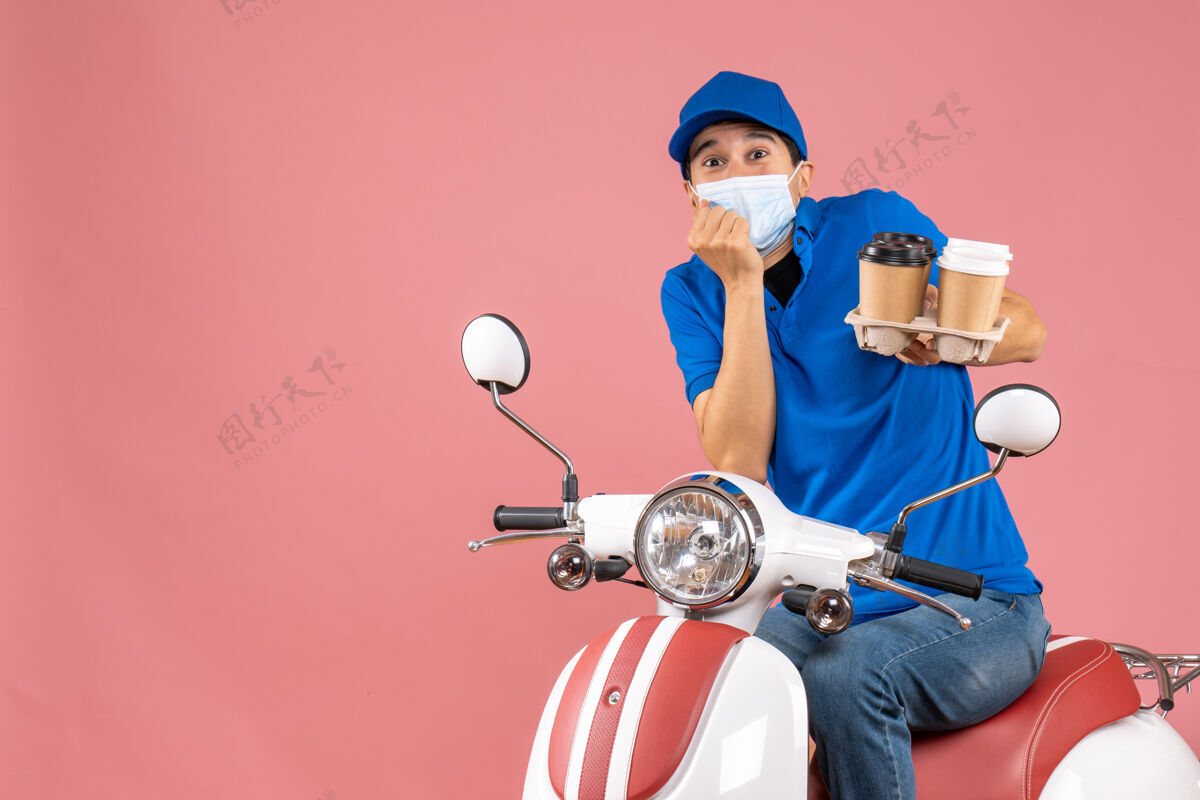 人上图：戴着帽子戴着面具的男性送货员坐在滑板车上送货 在桃色背景下感到惊讶滑板车送人