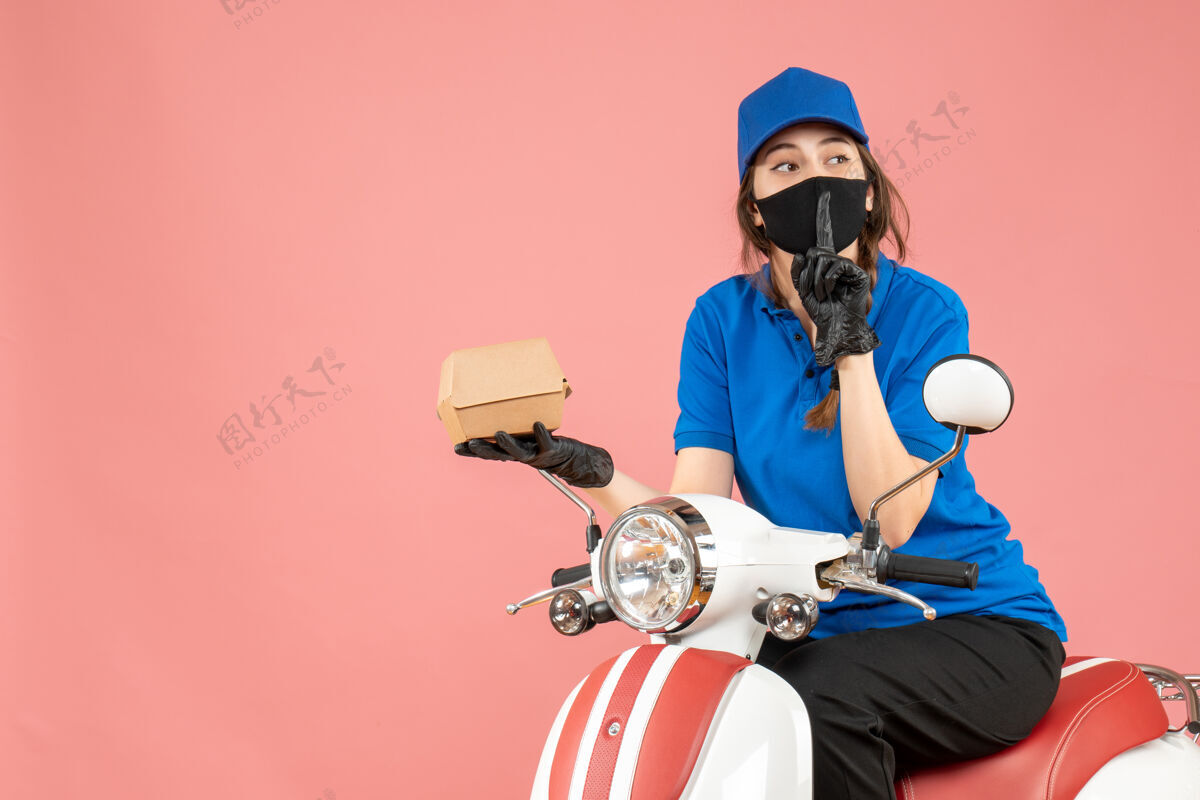 人俯视图：戴着医用面罩和手套的送货员坐在滑板车上 在柔和的桃色背景下 做着沉默的手势手势背景男