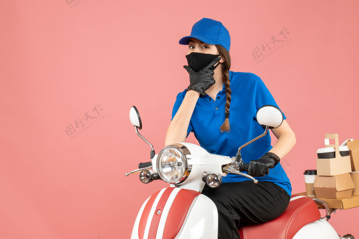 命令顶视图的快递女孩戴着医用面罩和手套坐在滑板车上传递粉彩桃背景的命令医疗背景手套