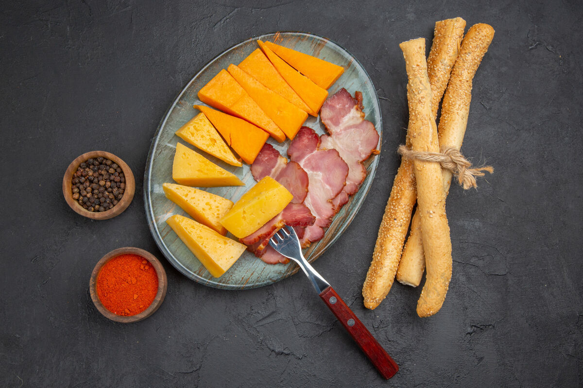 胡萝卜蓝色盘子上美味的香肠和奶酪片的俯视图黑色背景上的辣椒一餐蔬菜胡椒