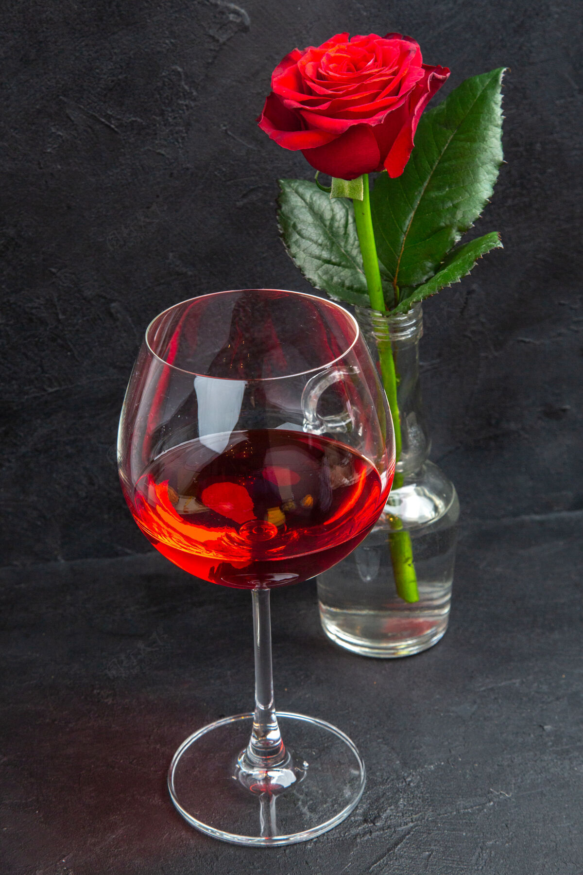 高脚杯正面近距离观看盛水和红酒的黑底花瓶中的红玫瑰液体酒背景