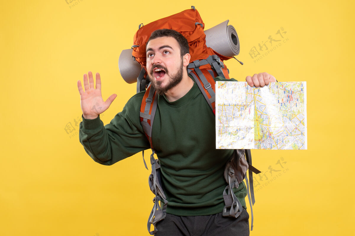 年轻人顶视图年轻的微笑旅行的家伙背着背包拿着地图 并显示黄色的五个地图视图成人
