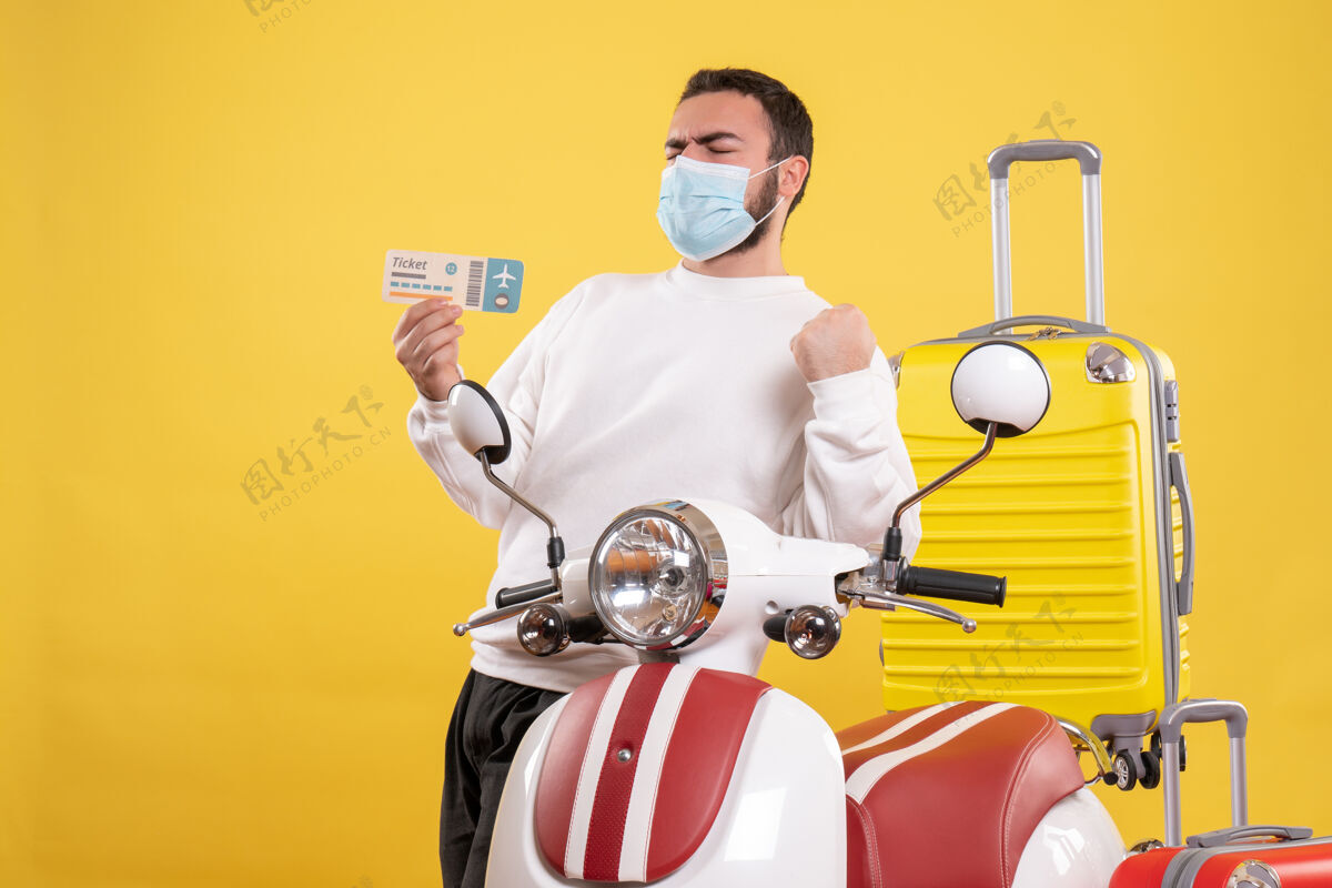 手提箱旅行概念的俯视图 戴着医用面罩的骄傲的家伙站在摩托车旁边 黄色手提箱在上面 手里拿着车票顶部自动装置视图