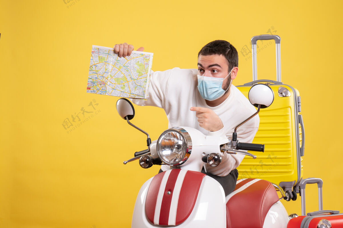 旅行旅行概念的俯视图 戴着医用面罩的年轻人站在摩托车旁 黄色手提箱放在上面 拿着地图朝上年轻人地图黄色