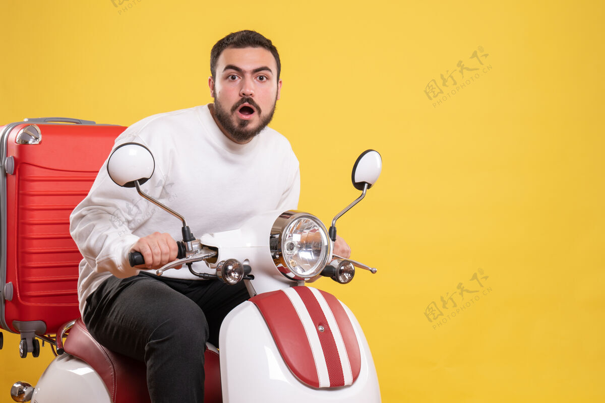 运动俯视图是一个惊讶的年轻人坐在摩托车上 手提箱放在黄色的上面车辆年轻人摩托车