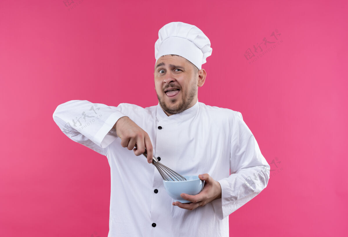 年轻年轻帅气的厨师穿着厨师制服 拿着碗和威士忌孤立地站在粉红色的墙上厨师碗威士忌