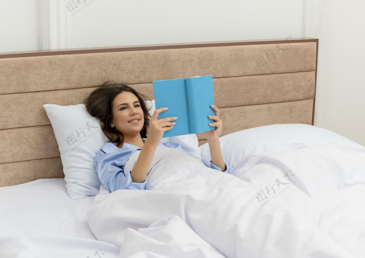 床穿着蓝色睡衣的年轻美女躺在床上看书休息 在卧室里享受周末室内背景卧室