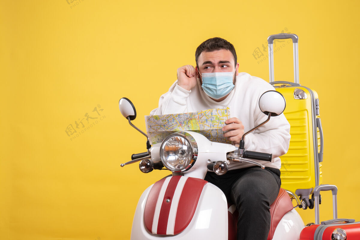 面罩带着医用面罩的好奇的年轻人坐在摩托车上 带着黄色的手提箱 手里拿着地图男人足球摩托车